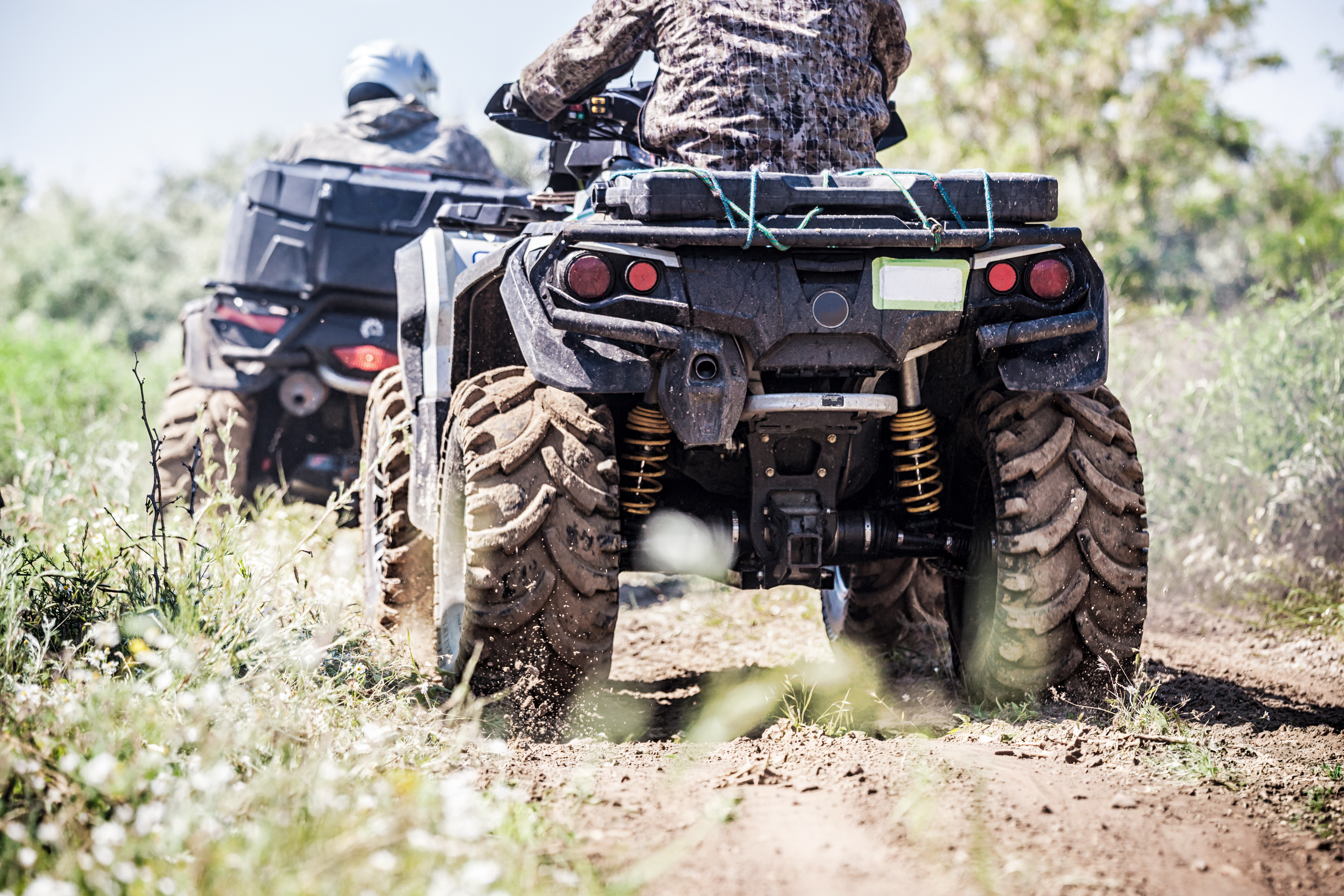Two people riding all terrain vehicles.