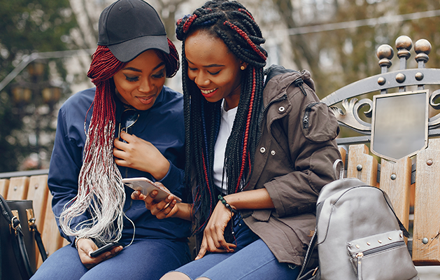 Two women on a park bench looking at a cell phone.